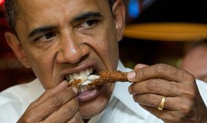Obama bites down on a fried frog leg, grimacing with his teeth showing.